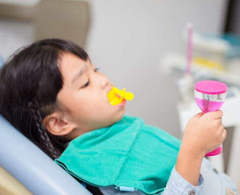Child in dental bib blowing bubbles during dental visit at Breezy Point Smiles office.