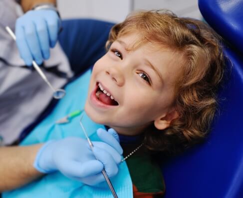 Young child smiling at dentist during examination with dental professional in blue gloves.