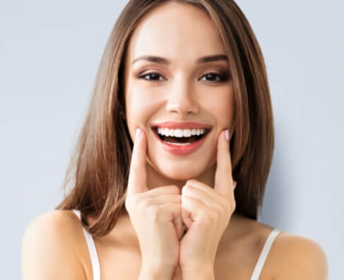 Smiling woman with fingers on cheeks against light background, representing dental care and happiness.