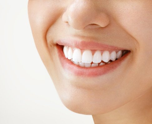 Close-up of person smiling brightly, displaying white healthy teeth against neutral background.