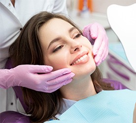 Woman receiving dental examination in dental office with gloved dentist hands touching face