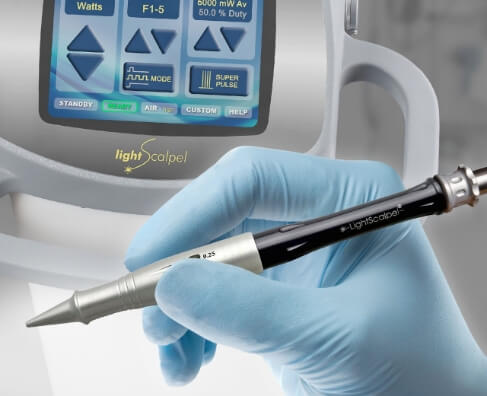 Gloved hand holding dental handpiece with ultrasonic scaler unit in background