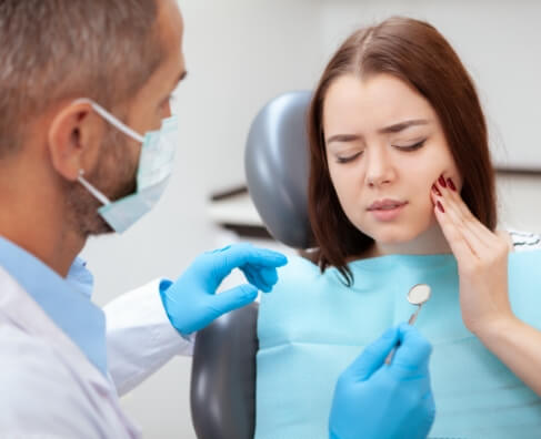 Dentist in mask and gloves showing patient X-ray results in dental office chair.