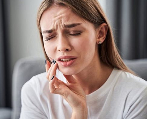 Woman with concerned expression touching her mouth, suggesting dental pain or discomfort in indoor setting.