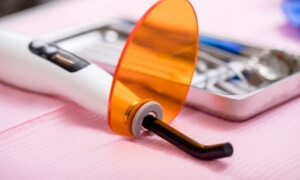 Amber-colored dental retainer displayed on pink surface with blurred dental office equipment background.