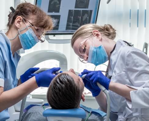 Two dental hygienists in masks and gloves treating a patient in a modern dental office.