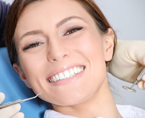 Woman smiling during dental examination with dentist tools and blue chair visible.