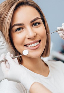 Young woman smiling during dental examination with dentist tools in clinical setting.