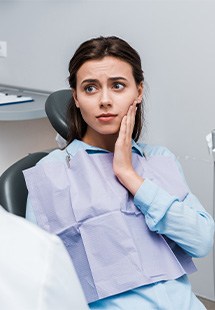Woman in dental bib touching cheek in pain at dental office chair.