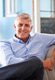 Smiling man in light blue shirt relaxing on couch near window
