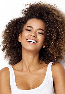 Woman with curly brown hair smiling warmly against white background in professional headshot.