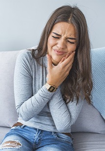 Woman with toothache holding her cheek, sitting on couch in discomfort