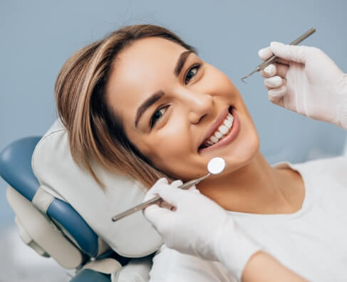 Woman in dental chair smiling while dentist holds tools during examination.
