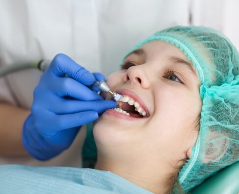 Child receiving dental examination from dentist wearing blue gloves in clinical setting.