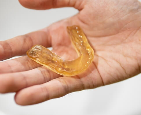 Hand holding clear yellow retainer or dental aligner against white background.