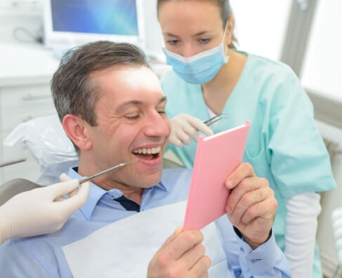 Dentist showing male patient pink mirror in dental office examination room