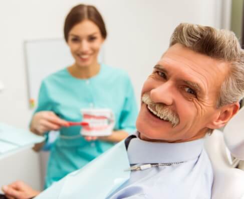 Dentist showing dental model to smiling patient in clinical office setting.
