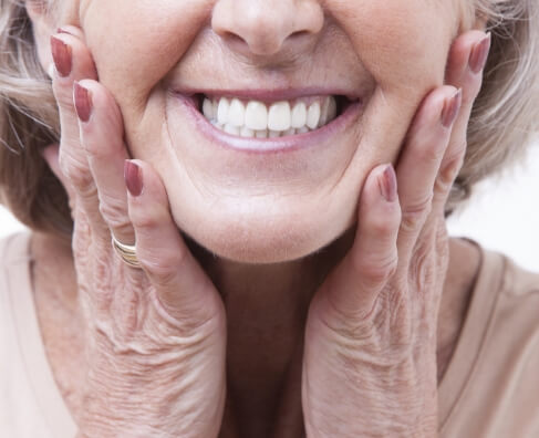Smiling older woman with gray hair touching her face against white background