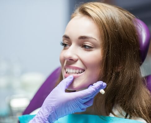 Woman smiling during dental examination with dentist in purple gloves at dental office.