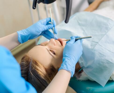 Dentist in blue gloves examining patient's teeth during dental procedure in clinical setting.