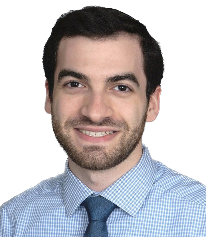 Professional headshot of a smiling man in light blue checkered shirt and tie against white background.