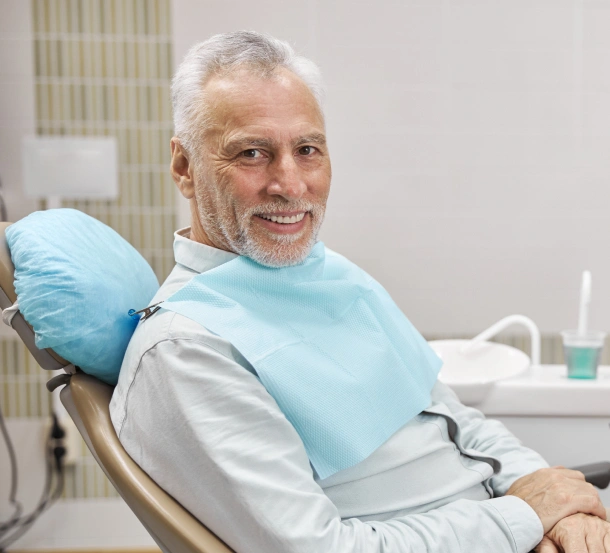Senior man smiling in dental chair wearing bib at Breezy Point Smiles office.