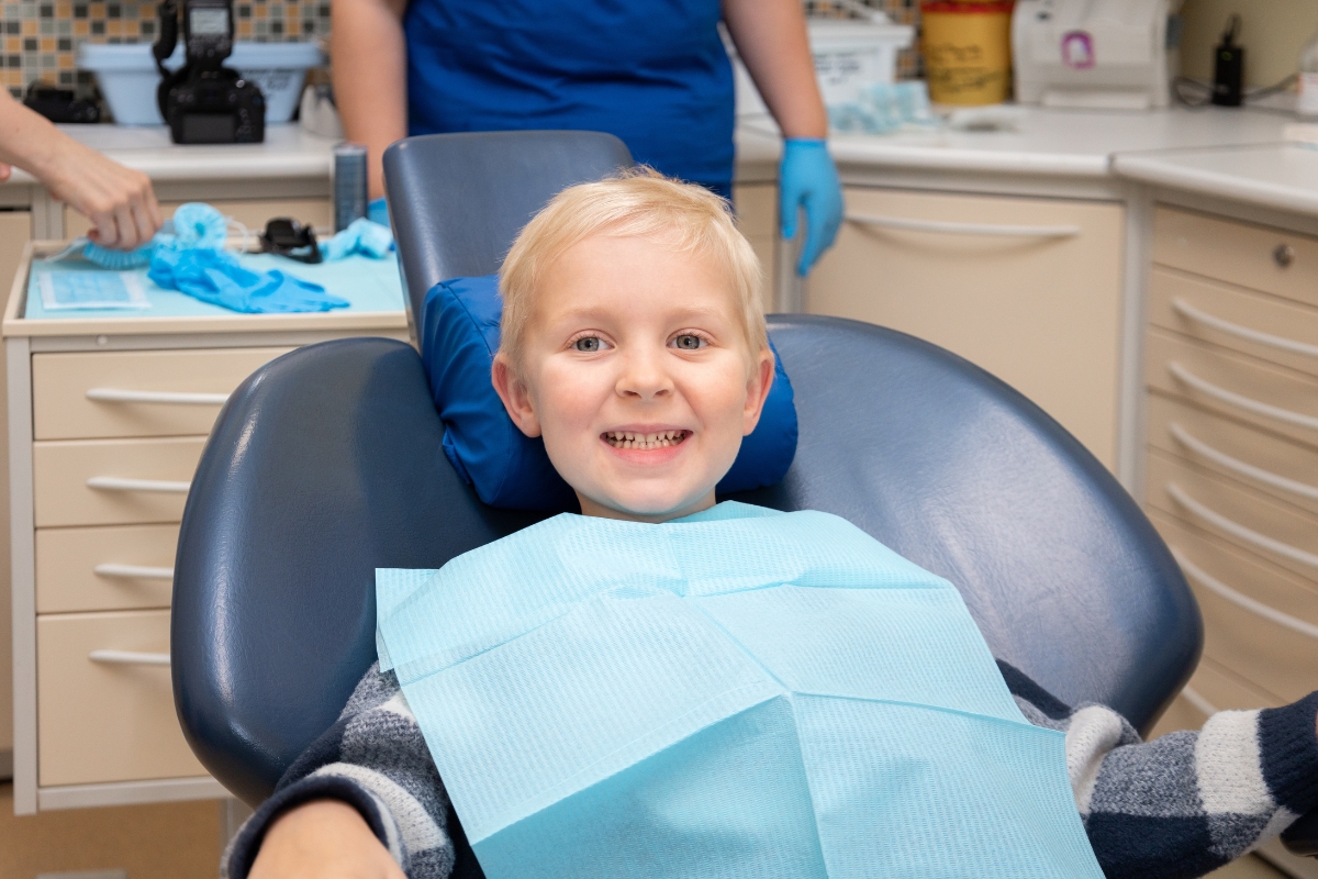 Dentist checking a smiling toddlers teeth in dental chair