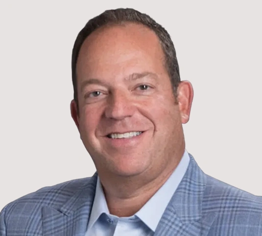 Professional headshot of smiling man in blue checkered shirt against neutral background