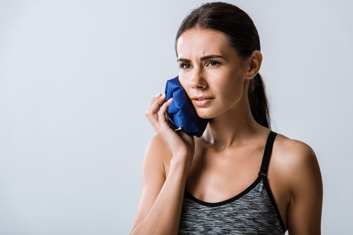 Woman holding an ice pack against her cheek due to dental pain.