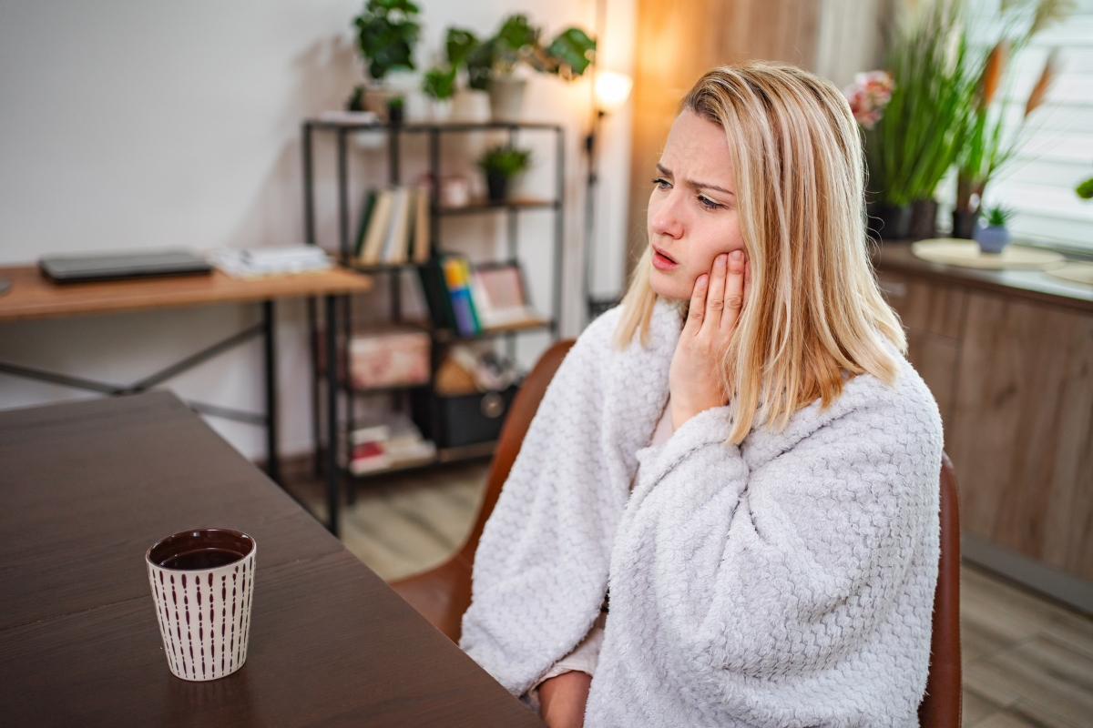 Woman holding cheek in pain from sudden tooth sensitivity overnight