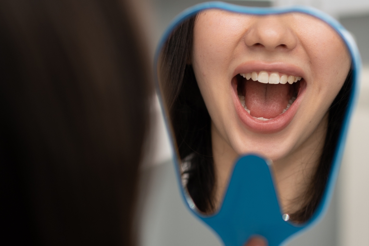 Woman checks open smile in mirror for uneven teeth and cosmetic solutions